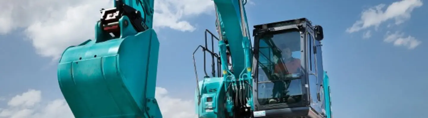 Operator driving an excavator digging soil at a construction site with safety barriers in the background.