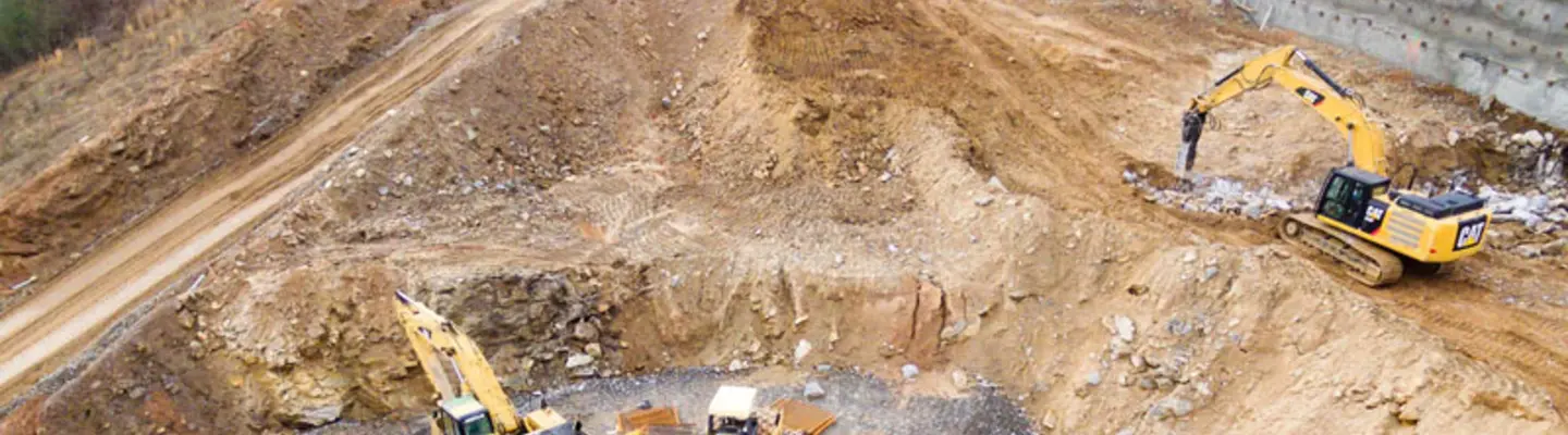 Excavators assisting construction crews on-site, with safety barriers in place to control access and protect workers.