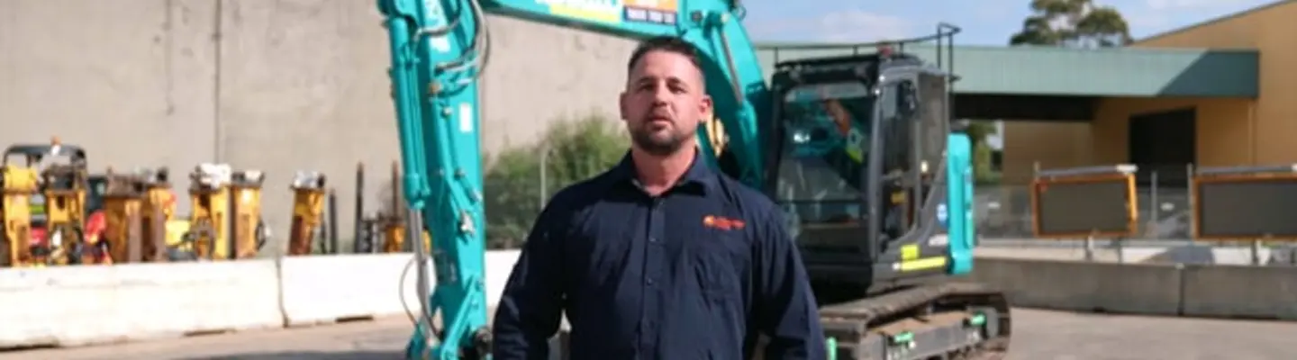 A construction worker standing in front of an excavator near temporary barriers at a worksite, highlighting safety practices.