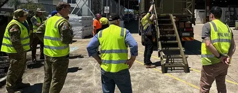 Personnel modifying a large container on a truck in an industrial yard.