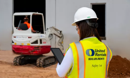 woman on jobsite holding ipad next to skid steer