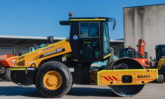 Standby compaction roller parked near construction barriers, ready for ground stabilization work on the site.
