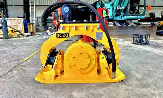 Plate compactor machine on a construction site near safety barriers, used for compacting soil and maintaining ground stability.