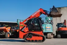 Man operating a wheel loader moving dirt at a construction site with safety barriers visible in the background.