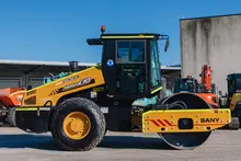 Standby compaction roller parked near construction barriers, ready for ground stabilization work on the site.