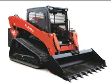 Track loader moving materials on a construction site with visible safety barriers and warning signs in place.