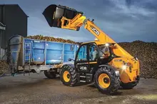 Man operating a telehandler on a construction site near safety barriers, lifting materials for site development.