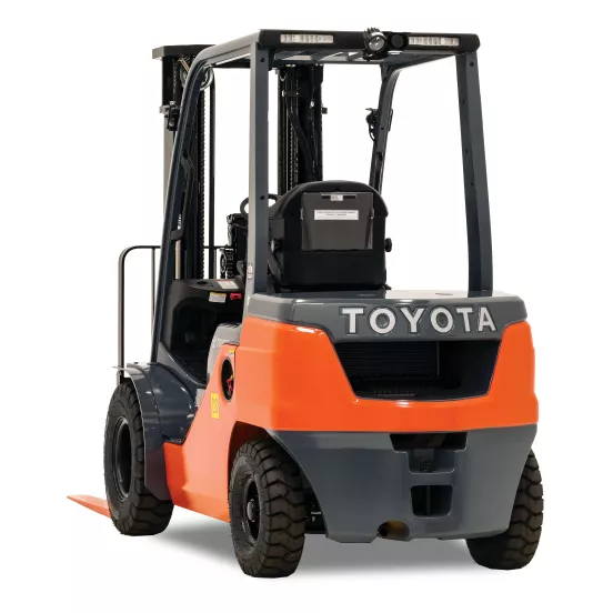 Rear view of orange and black Toyota warehouse forklift with black lifting mast and orange forks with an open cabin.